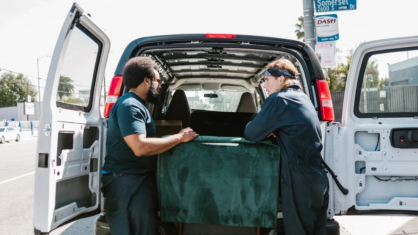 Two-person crew loading a couch into a full-service junk removal van, illustrating the labor-included nature of professional junk removal services